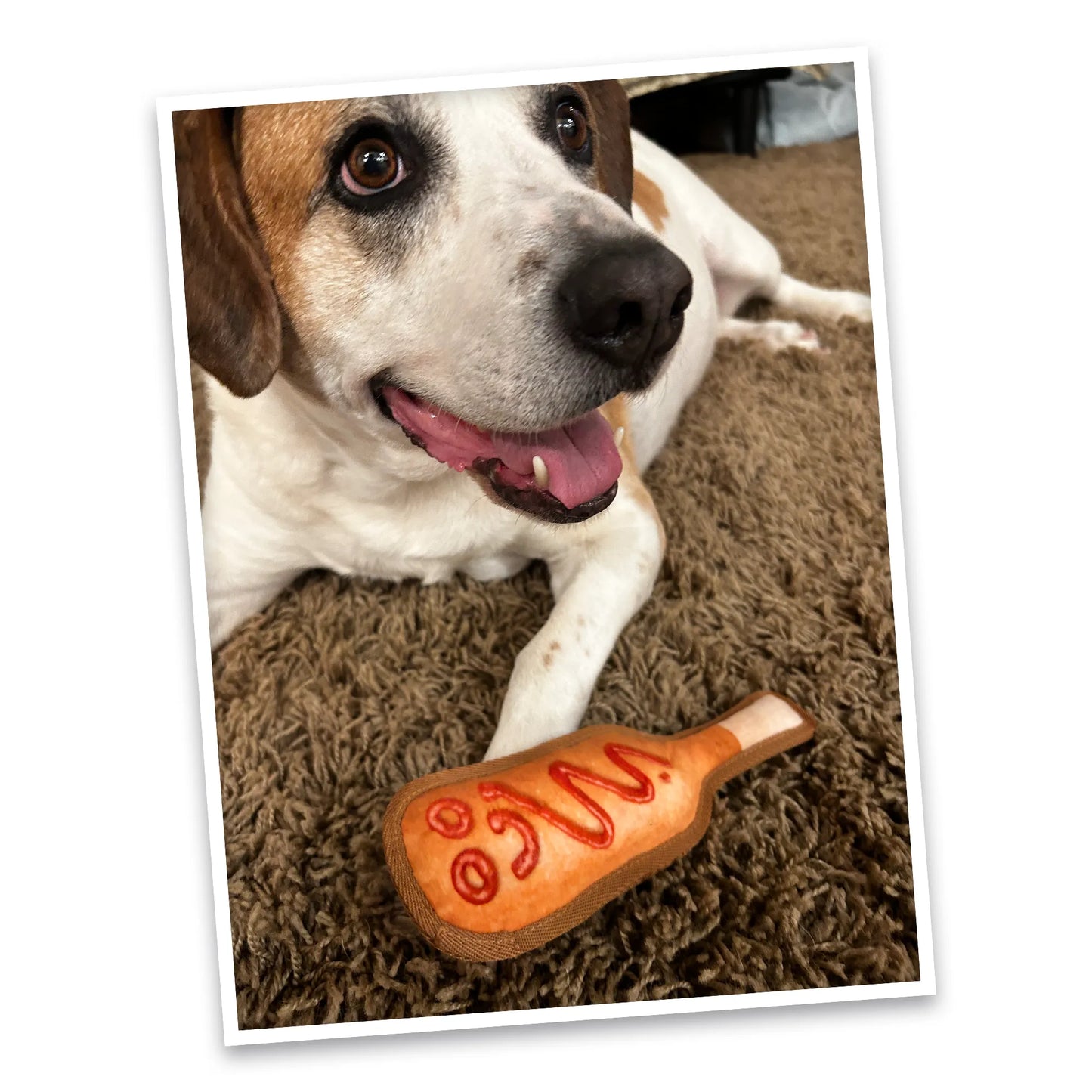 Happy dog lying next to the Tuffer Chewer Mini Corn Dog toy, looking excited to play.